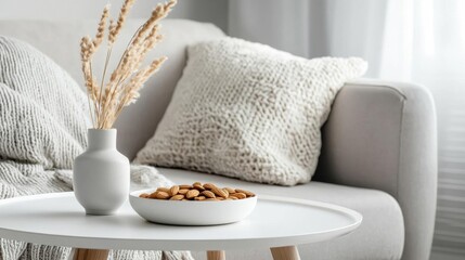 Modern living room with a gray sofa and a white coffee table in front of it. on the coffee table, there is a white vase with dried pampas grass in it and a bowl of almonds.