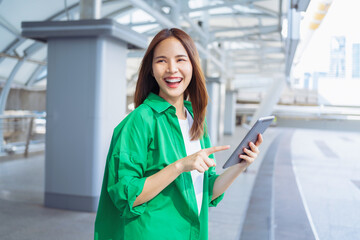 Smiling asian woman holding digital tablet while standing in front of modern business building