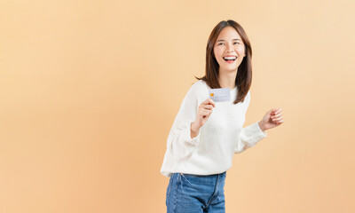 Cheerful beautiful Asian woman holding credit card isolated on beige color background.