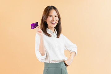 Cheerful beautiful Asian woman holding credit card isolated on beige color background.