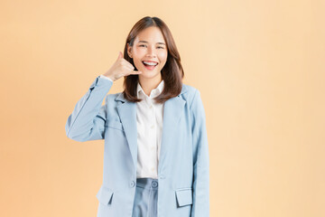 Cheerful Asian businesswoman makes a call me gesture against a beige background.