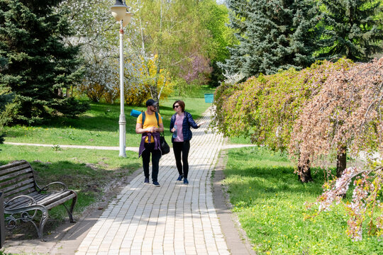 Two people walk on a path in a vibrant spring park, surrounded by green grass, blooming trees, and colorful flowers. Enjoying the sunny day and nature together.