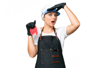 Butcher woman wearing an apron and serving fresh cut meat over isolated chroma key background doing surprise gesture while looking to the side