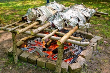 Outdoor Fire Pit with Foil-Baked Meat. Barbecue Meat Wrapped in Foil Over Glowing Coals.