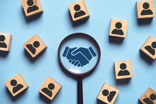 This image highlights the importance of collaboration and partnership, featuring a handshake within a magnifying glass surrounded by blocks symbolizing people.