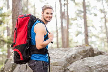 Adult male hiker standing on outcrop smiling in pine forest carrying red black backpack, copy space