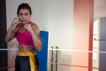 Female athlete standing in boxing ring raising fists wearing pink sports bra black shorts