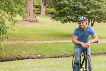 Fototapeta premium Man leaning on black bicycle wearing multi-color helmet near dirt walking path in park, copy space