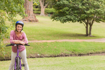 Woman leaning on purple bicycle handlebars in park wearing blue helmet, copy space