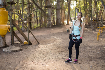 Woman navigating rope course in forest wearing harness with carabiners, gloves, copy space
