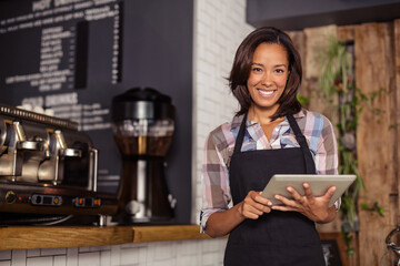 African American woman holding tablet and smiling at cafe counter with espresso machine, copy space