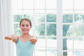 School-age girl in blue top extending arms horizontally at home by multi-pane window, copy space