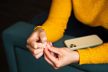 Woman ripping and picking on cuticle skin peeling during waiting for important notifications on...