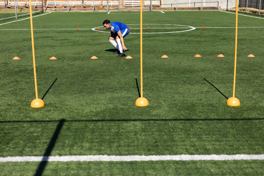 Male soccer player in sportswear performing agility drill on turf field with slalom poles and cones - Powered by Adobe