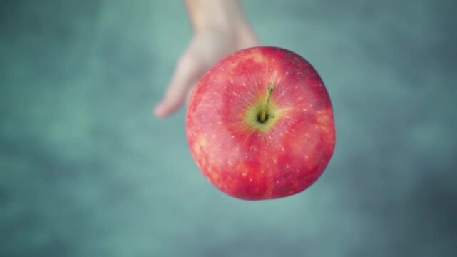Close-up of a hand holding a ripe red apple aloft.