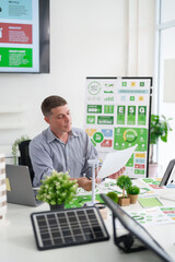 Adult Caucasian man analyzing ESG reports and green business strategies focusing on carbon reduction sustainable energy solutions and environmental impact in a modern office setting