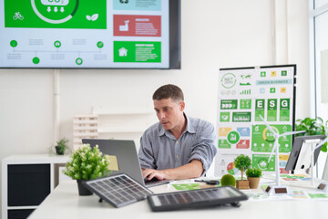 Dedicated adult male professional analyzes ESG data in a modern green business office driving...
