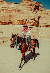 Bedouin man riding horse through desert landscape near Petra, Jordan