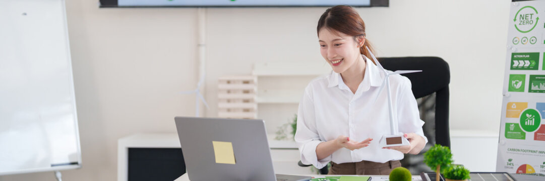 Asian young adult woman presents wind turbine model on video call discussing green business and ESG sustainable energy solutions for net zero carbon reduction initiatives