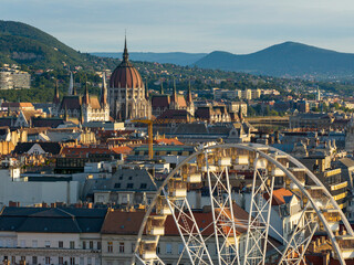 Roof of Budapest with a part of giant ferris wheel and Hungarian Parilament's building towers. mountains on the background