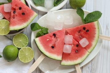 Watermelon slices, limes and mint in white plates, top view. Ripe watermelon pieces on sticks,...