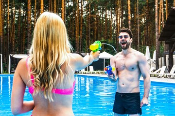 Loving couple staying in the swimming pool outdoor while playing with water guns, having fun. Summer vacation, active leisure, lifestyle concept