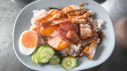 Red pork and crispy pork on rice in a blue plate on a   table in Thailand