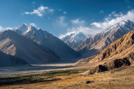 Golden sunlight casts long shadows across the dramatic Nubra Valley landscape, revealing rugged mountain textures and snow-capped Himalayan peaks under a vast blue sky in northern Ladakh