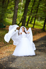 A bride is walking down a road in a white dress with a veil