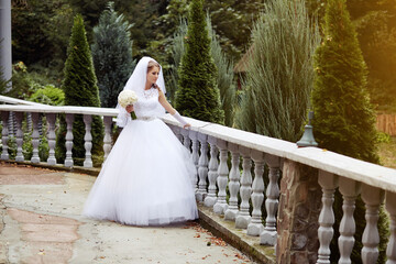 A bride is standing on a balcony, holding a bouquet of flowers