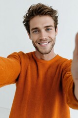 Smiling Man Selfie: A young man with a warm smile and stylish, tousled hair takes a selfie in an orange sweater. His joyful expression is infectious. 