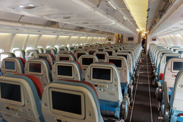 Rows of empty seats are visible within the airplane cabin, highlighting the airline's seating arrangement and onboard amenities. Soft lighting and a narrow aisle create a calm atmosphere.
