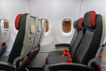 Rows of empty airplane seats are visible along the cabin wall, with large windows allowing a view outside. Seatbelts are unfastened, creating a calm atmosphere before departure.