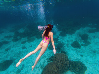 A swimmer explores a vibrant coral reef while scuba divers observe nearby. Sunlight filters through the clear water, illuminating this underwater paradise filled with marine life.