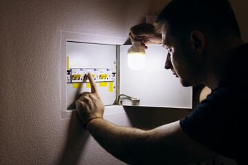 Power outage. A man holds an LED lamp in front of an electrical panel.