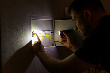Power outage. A man holds an LED lamp in front of an electrical panel.