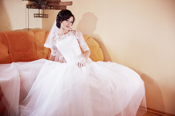 A woman in a white wedding dress is sitting on a couch