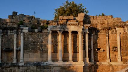 Stone columns and wall remains of an ancient amphitheater in a Mediterranean town. Historical...