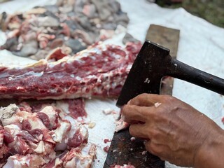 A butcher chops fresh beef with a cleaver on a wooden board at a traditional outdoor market.