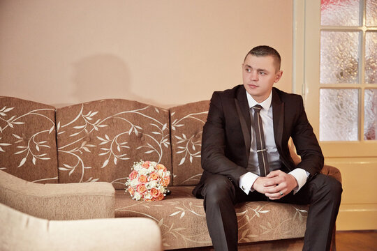 A man in a suit sits on a couch with a bouquet of flowers in front of him
