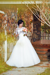 A woman in a white dress is standing in front of a stone wall with a bouquet of