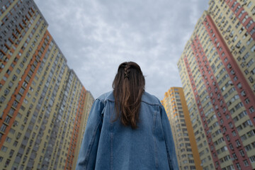 A young woman with long hair gazes up at the towering high-rise buildings in a vibrant...