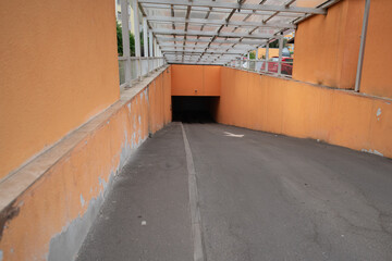 A sloping concrete ramp descends toward a dark opening, framed by an orange wall and covered by a...