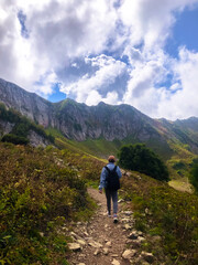 Man with a backpack hiking along the Path of Health trail at Rosa Khutor resort in Sochi, Russia, seen from behind. Concept of outdoor adventure, active travel, and exploring alpine landscapes