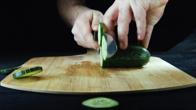 Close-up of hands slicing a cucumber on a wooden cutting board.