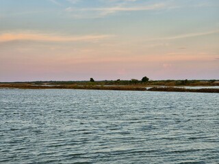 Calm water surface with distant shoreline and pastel evening sky over .