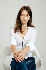 Teenager sitting confidently in a stylish outfit against a plain backdrop