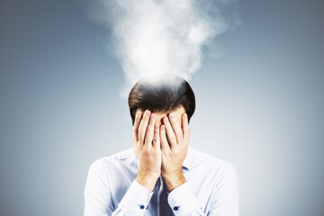 Frustrated businessman under pressure with smoke rising from head symbolizing burnout and stress in corporate job environment, studio shot.