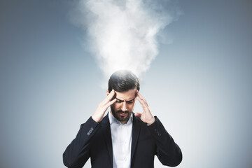Stressed businessman under pressure with smoke rising from head representing burnout and overwork...