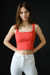 Teenager in a red top and white jeans poses confidently against a dark background